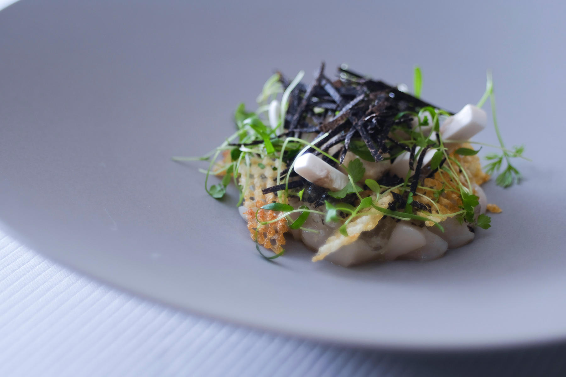 2019年、冬。黒トリュフコースは、この料理から始まる。岩手県産の新鮮かつ甘みのある泳ぐホタテは、その旨味を引き出すため、オリーブオイルと塩、胡椒のみのシンプルな味付けに。そこにキャラメリゼした玉葱の甘みをプラス。細切りにしたトリュフの香りとのマリアージュが楽しい。食べやすさと一体感が光る。