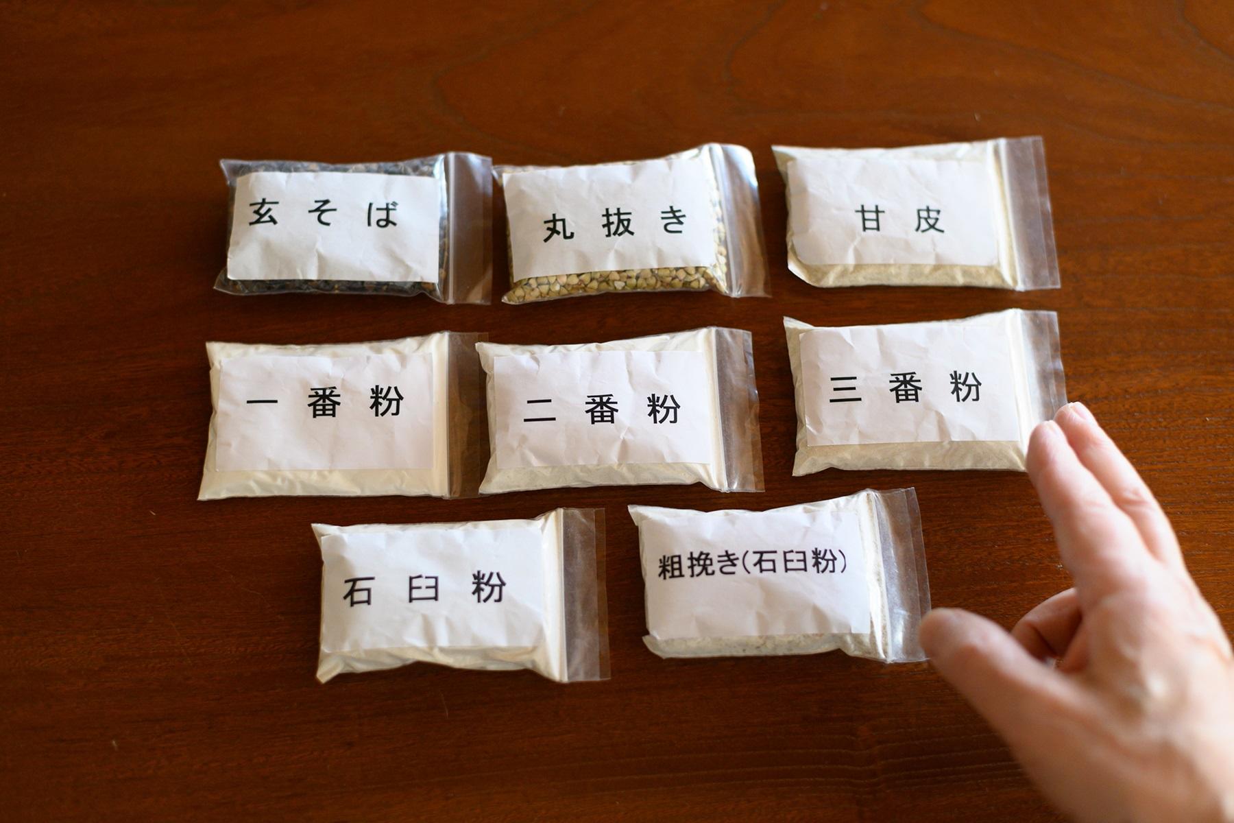 挽き方で味が変わるのも蕎麦の面白さ。一段目は左から殻がついたままの実である“玄蕎麦”、外皮の黒い殻をとり、甘皮が付いた“丸抜き”、甘皮だけを挽いた“甘皮”。二段目は更科粉と呼ばれる内層粉の“一番粉”、中層粉の“二番粉”、甘皮ごと挽いた“三番粉”。三段目の“石臼粉”と“粗挽き”は石臼の挽き目の違い。