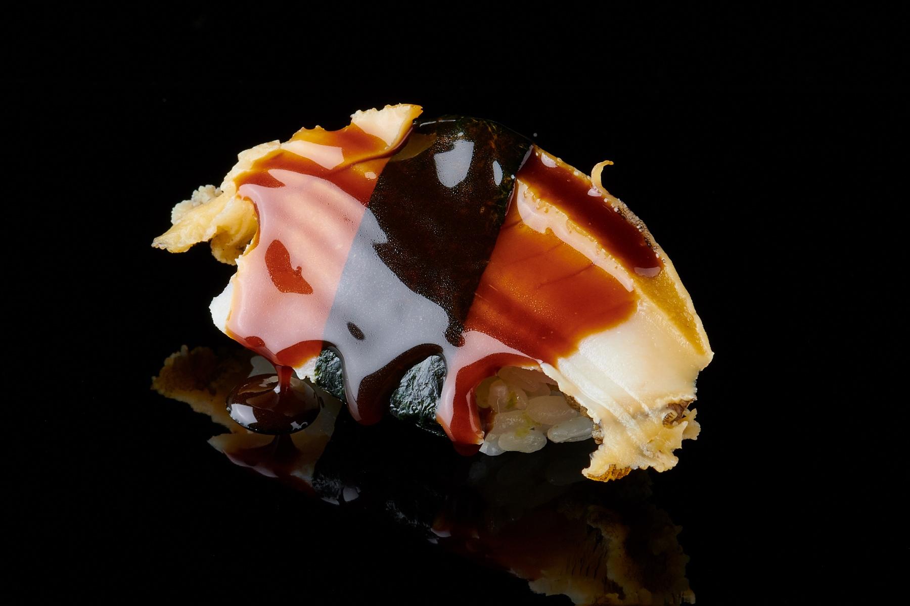 マダカ鮑を用いる握り“蒸しあわび”。酒酒、水、塩で1時間30分ほど煮て味を煮含め、ツメを塗り、海苔をひと巻して供する。鮨種の木札がかかっていたら、ぜひ頼みたいところ。