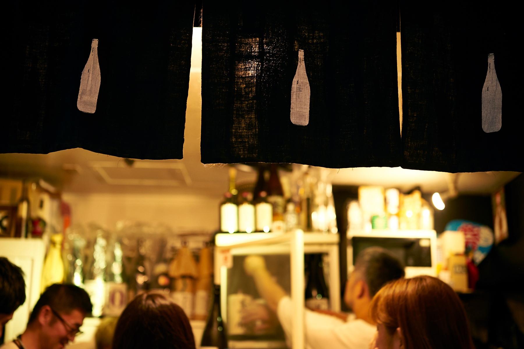 酒瓶を染め抜いた暖簾が「こっちの酒は旨いぞ」と手招きします。