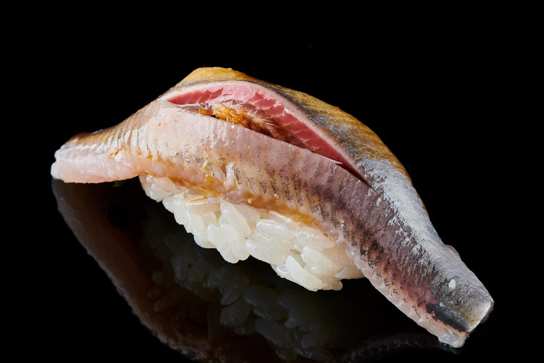 片身で1貫を握った、鰯の握り。中に、おろし生姜とあさつきが入る。