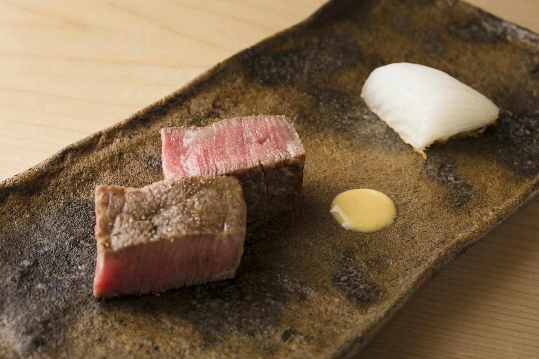 5月の献立から焼物の「牛ヒレ肉炙り　新玉ねぎフライ」。新玉ねぎは衣をつけて油で揚げてから、衣をはずして盛りつける。瑞々しい甘味が際立つという。牛肉の炭火焼きは盛りつけもシンプルに、溶き辛子を添えて。素材のもつ力強さがストレートに伝わってくる。