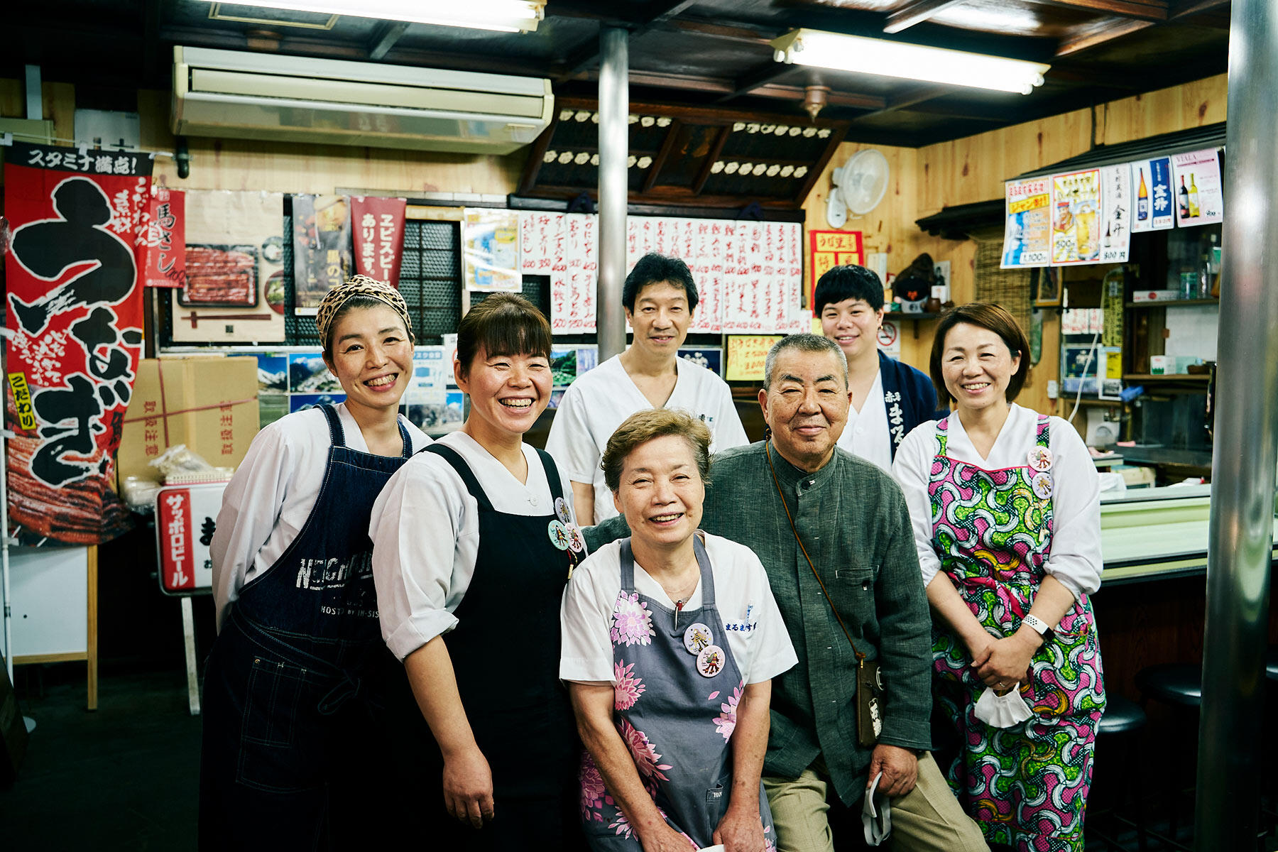 笑顔が絶えない、まるます家ファミリー。前列右から時計回りに、長女の松島和子さん、二代目の石渡勝利さん、奥様の宏子さん、次女の石渡利子さん、三女の塩川玲子さん、次女の夫で鰻の焼き担当の博幸さんと息子の龍之介さん