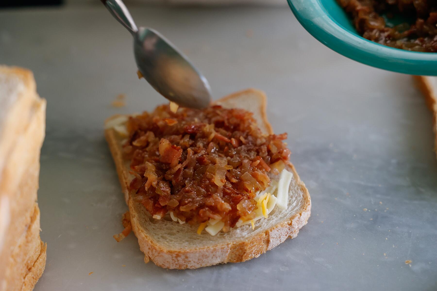 パンにチーズとベーコンジャムをはさむ