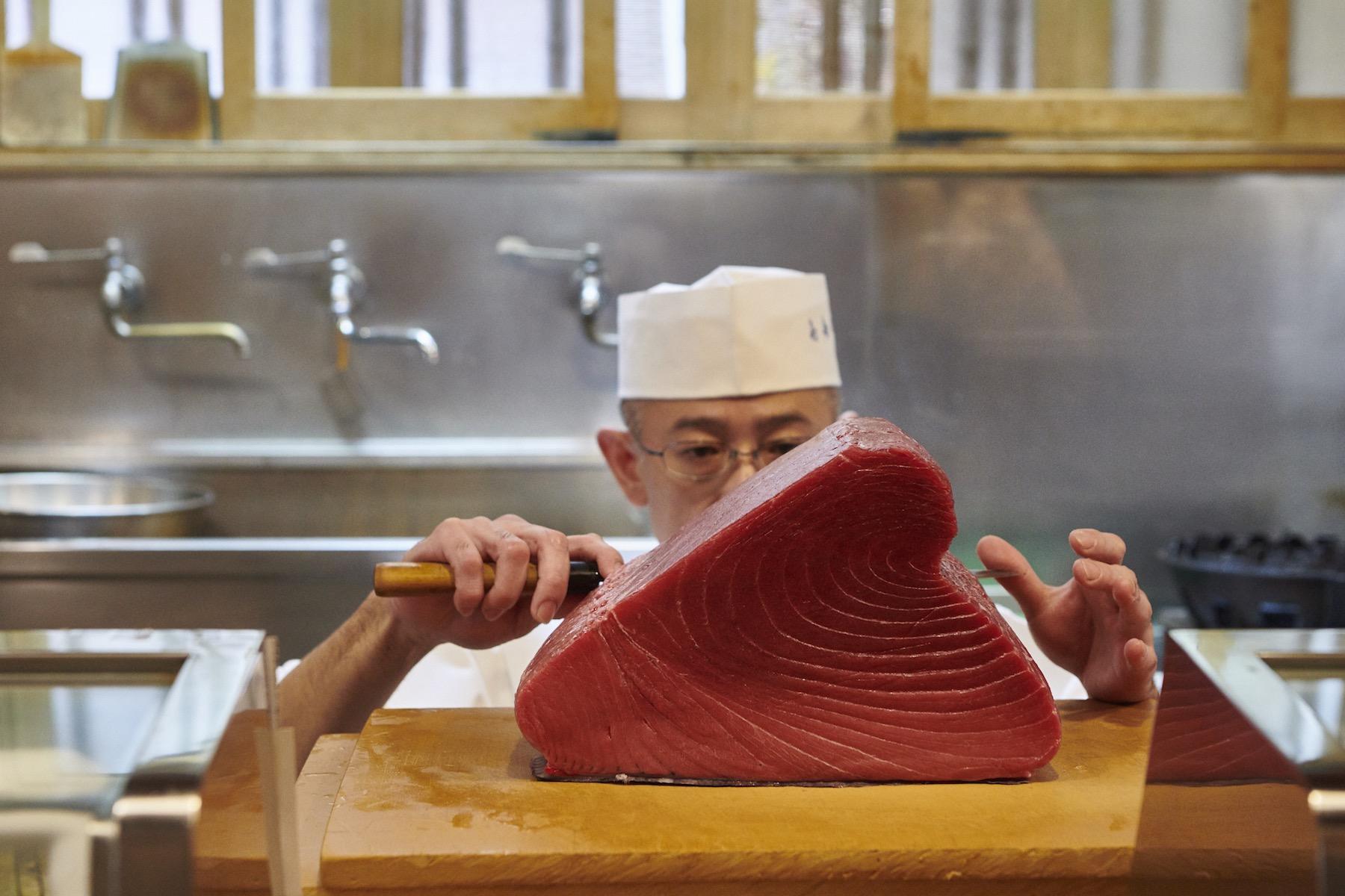 仕入れたマグロを真剣な面持ちで、状態を見極めながら切り分ける四代目。この後、上部のくびれた部分にまな板と平行した角度で包丁を入れた。